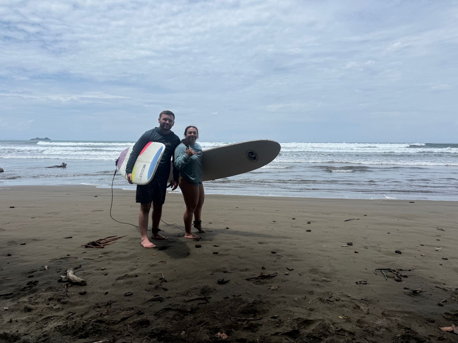 Dr. Dakota and his wife with surfboards on a beach abroad